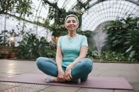 An older lady sitting cross-leg on a yoga mat.